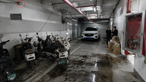 生成高清现实风格图片：现代地下车库（广角），一辆电动车正在飞线充电，电线横穿人行通道。旁边通道拐角处有车辆违规停放在防火卷帘门下。墙角消火栓箱玻璃破损，内部水带缺失。
10 处隐患对照：
五辆电动车停放混乱
1 根电线头从天花板上垂落。
SUV 违规停放在防火卷帘下方。
消火栓玻璃破损。
消火栓箱内水带缺失。
角落堆放纸箱等易燃品。
地面有大片油污。
有两名行人在车库易燃品旁吸烟。
安全出口标志灰色的，不亮。
烟感保护罩未去除。